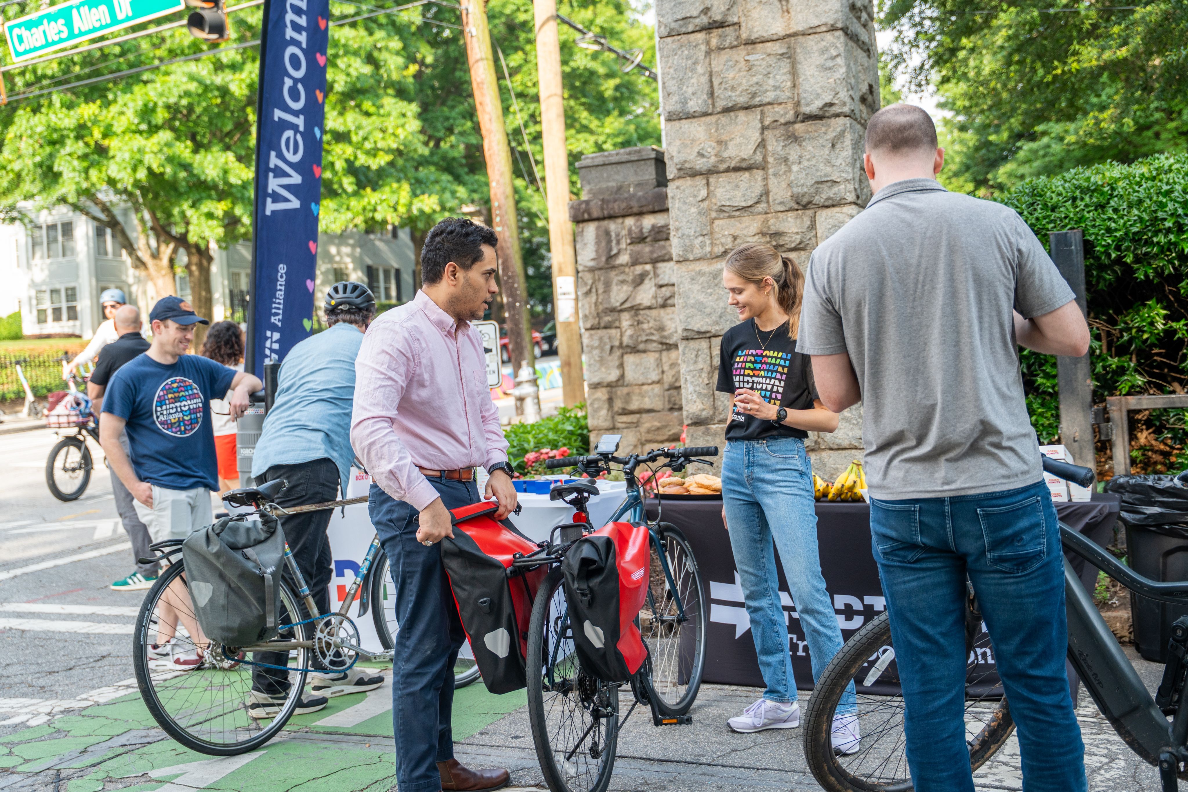 A group of bicycle commuters stands on the sidewalk talking with staff