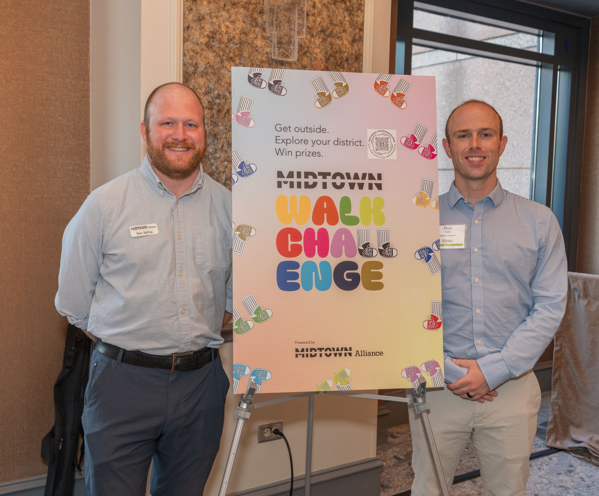 Two commuting experts standing next to a sign discussing the Midtown Walk Challenge