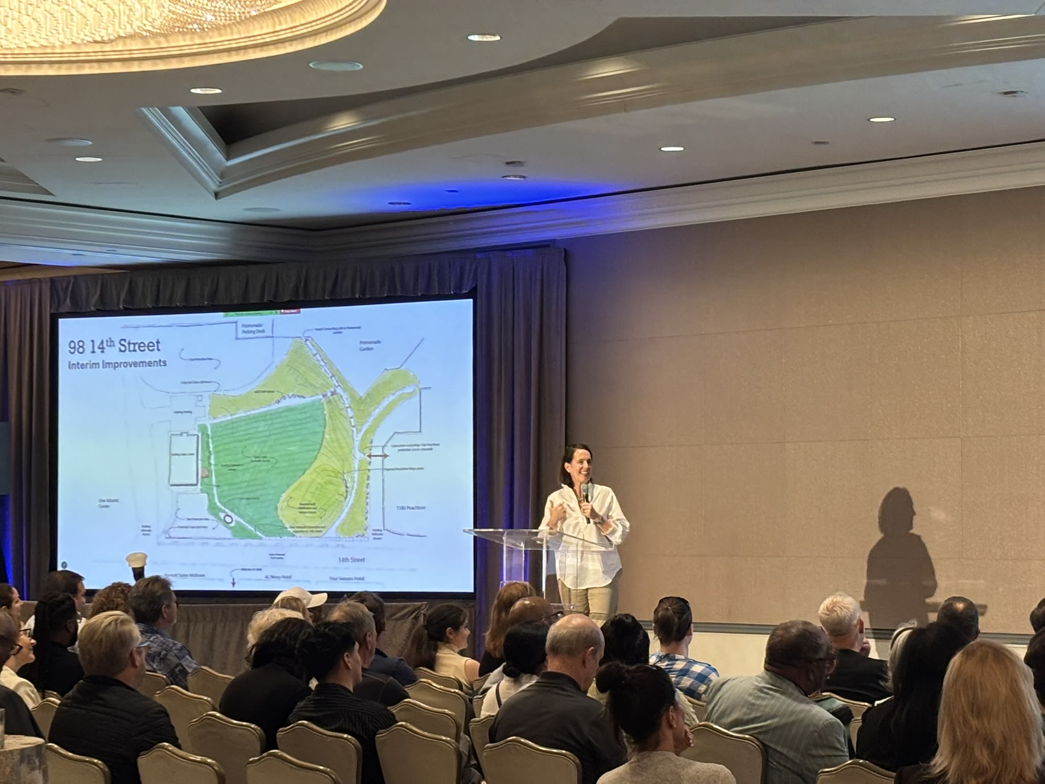 A crowd of people listen as a presenter discusses plans for the park